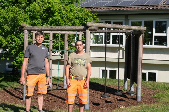 Zwei Männer in Arbeitskleidung vor einem Klettergerüst.