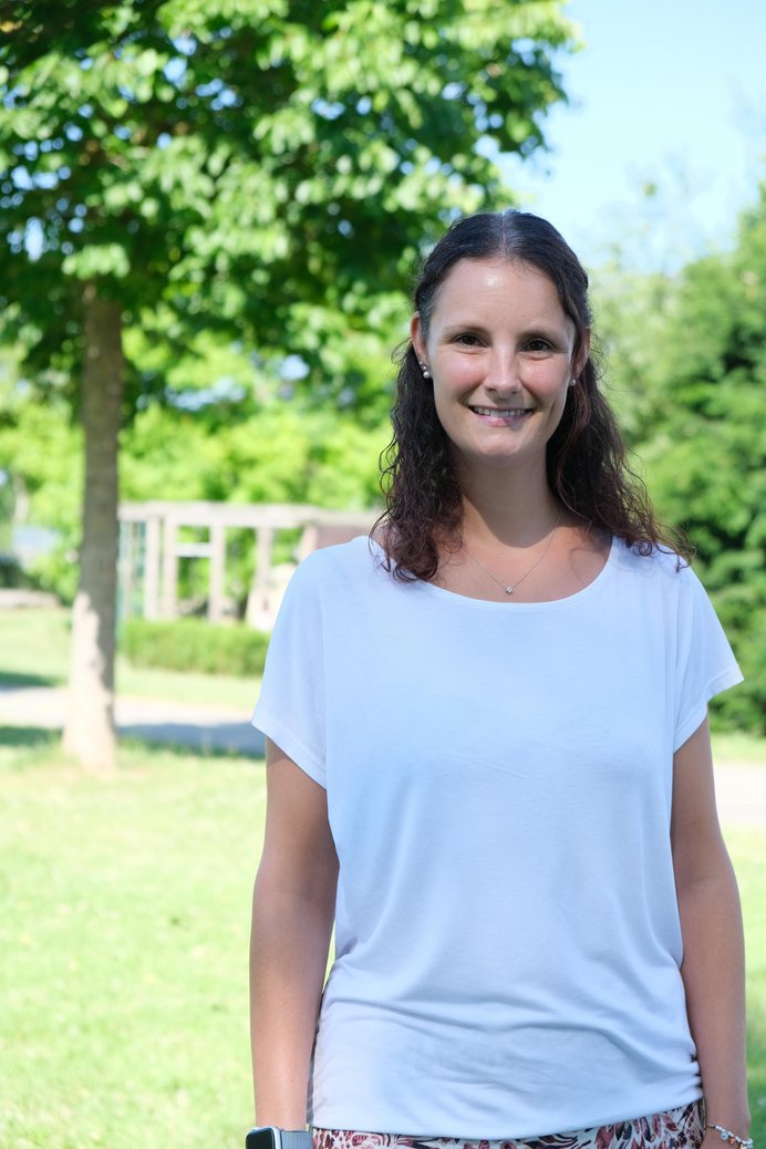 Frau mit braunen halblangen Haaren und weißem T-Shirt im Freien.